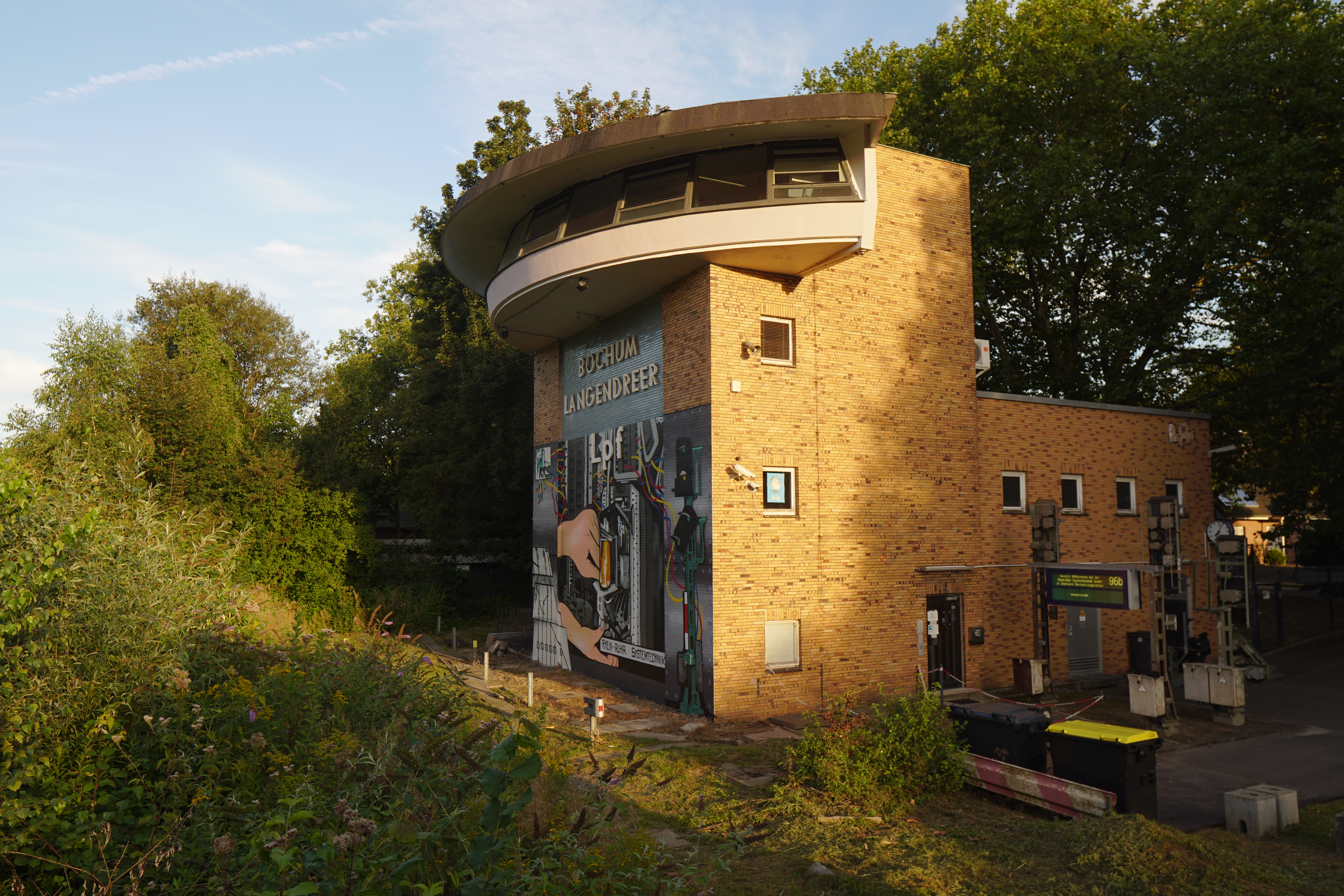 Ein Stellwerksgebäude mit einer halbrunden Kanzel und der Aufschrift &lsquo;Bochum Langendreer Lpf&rsquo;. Die Vorderseite ist bemalt mit Kabeln, Relaisanlagen und einem Signal. Vor dem Eingang steht ein Abfahrtsanzeiger und einige Signalanlagen.